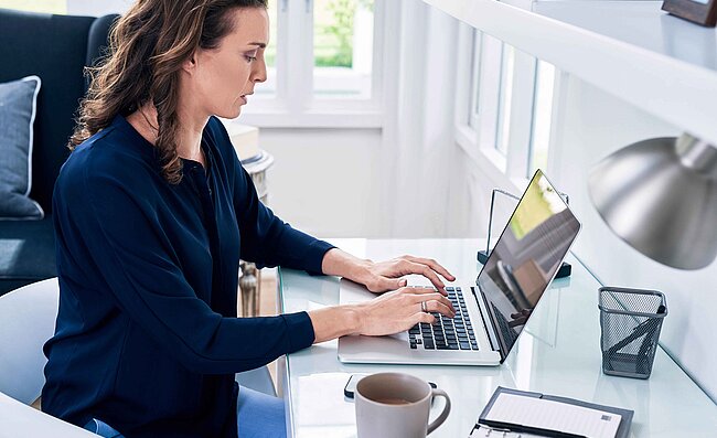 
			A woman in an office sitting at her laptop