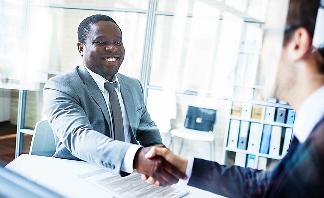 Two men sitting opposite each other in an office and shaking hands