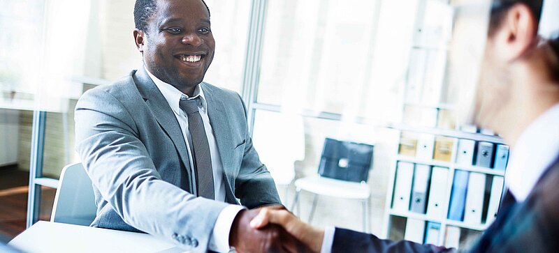 
		  Two men sitting opposite each other in an office and shaking hands
