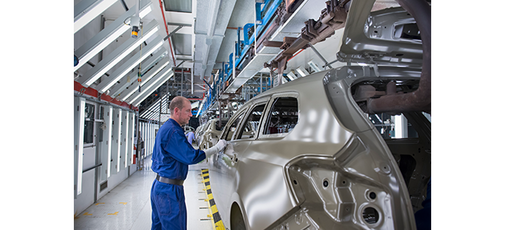 
				A man is working on a car on an assembly line.
