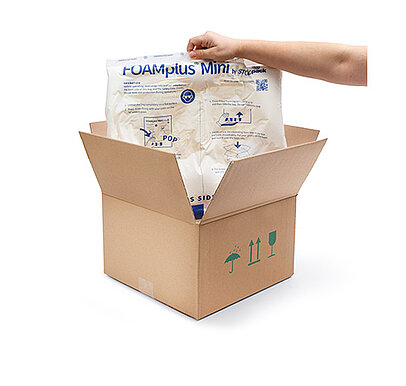 
			An arm holds up a FOAMplus Mini foam cushion that was previously placed in a cardboard box
