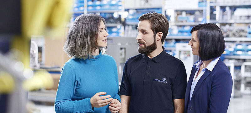 
		  Two women and a man talking in a factory