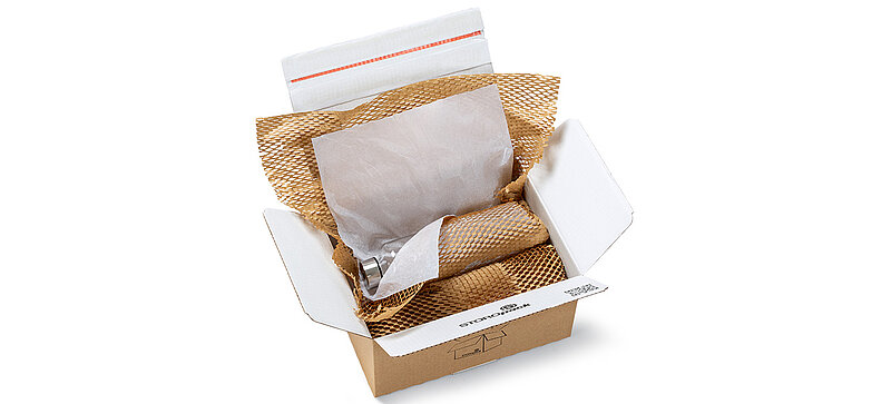 Ein Karton mit einer Flasche und anderen Produkten, die in braune und weiße Papierpolster eingewickelt sind.