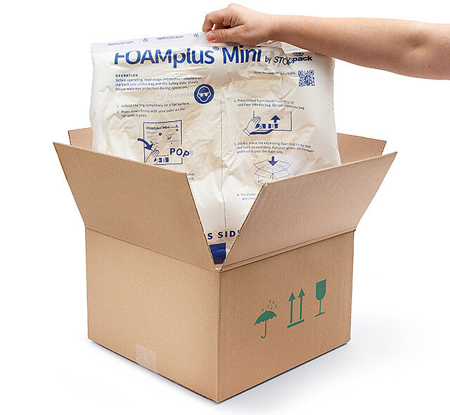 
			An arm is holding a FOAMplus Mini foam cushion that was previously inside a cardboard box