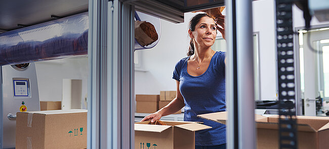 
			A woman packing products into a cardboard box at a packing station